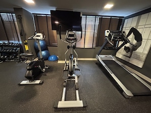 A gym with exercise equipment including a stationary bike, elliptical, treadmill, and weights. - Stgo Metro A. Hurtado - Domus Travels (Santiago)