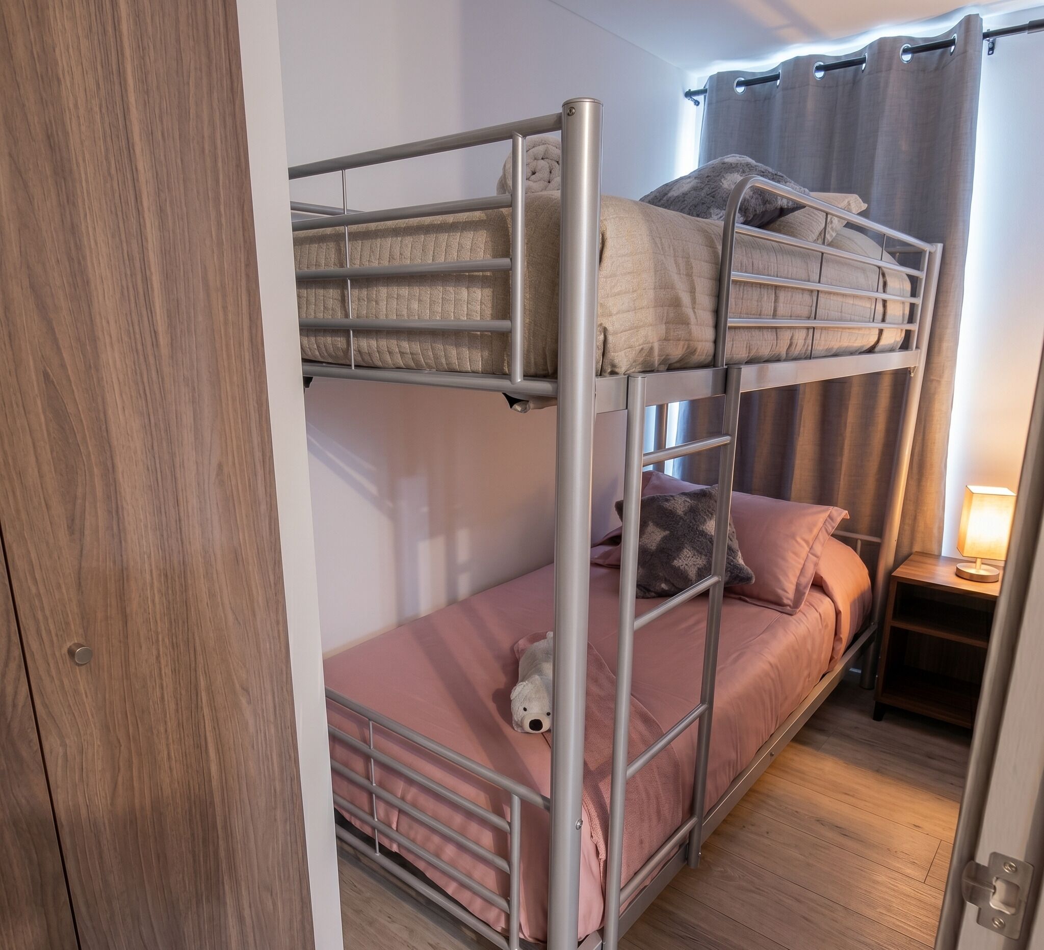 A bunk bed with a wooden wardrobe and a bedside table with a lamp.