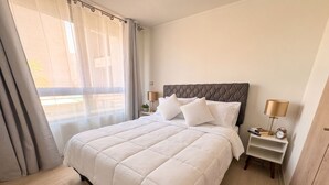 A hotel room with a large bed, two bedside tables, a window with curtains, and a view of the outside. - Stgo Metro A. Hurtado - Domus Travels (Santiago)