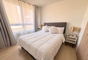 A hotel room with a large bed, two bedside tables, a window with curtains, and a view of the outside. - Stgo Metro A. Hurtado - Domus Travels (Santiago)