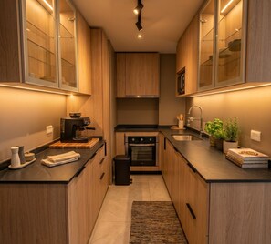 A modern kitchen with wooden cabinets, a built-in oven, a coffee machine, and a sink. - Eco Estación Santiago by Domus Travels (Santiago)