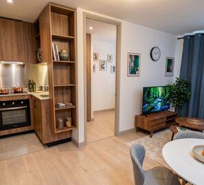 A modern kitchen with wooden cabinets, a built-in oven, and a dining area with a white table and chairs. - Stgo Metro A. Hurtado - Domus Travels (Santiago)