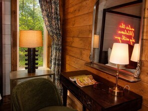 Ein Zimmer mit Holzwand, einem Vorhangfenster, einer Lampe, einem Spiegel und einer Zeitschrift auf einem Tisch.