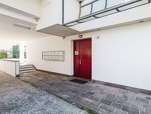 A building entrance with a red door, a mailbox, and a staircase leading up. - Caminito by Interhome (Riva del Garda)