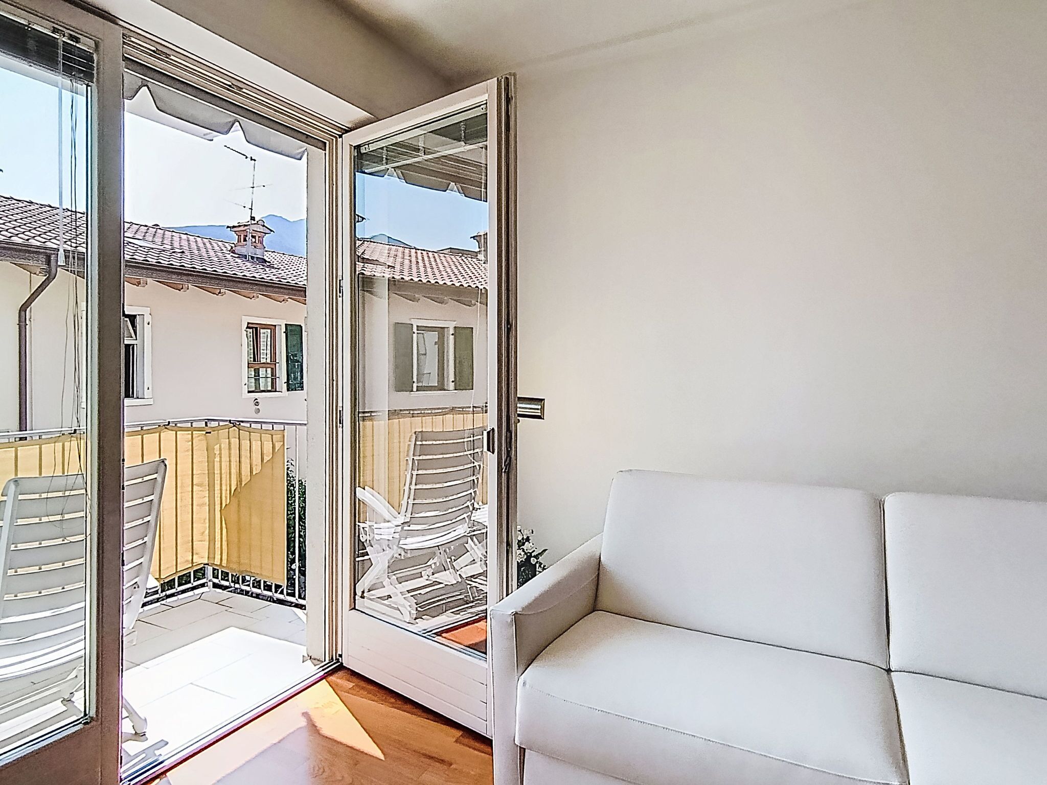 A balcony with a white sofa, a view of a building with a tiled roof, and a wooden fence.
