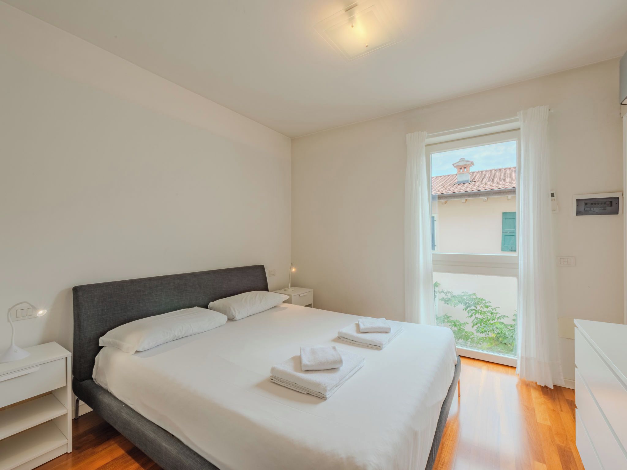 A bedroom with a bed, bedside tables, and a window with a view.