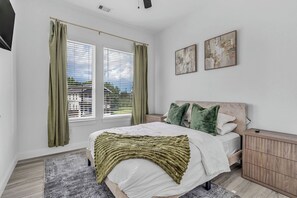 A bedroom with a bed, curtains, a bedside table, a nightstand, a headboard, and two wall-mounted artworks. - The Emerald Noir (Houston)