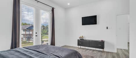 A bedroom with a bed, a ceiling fan, a TV mounted on the wall, and a sliding door leading to a balcony.