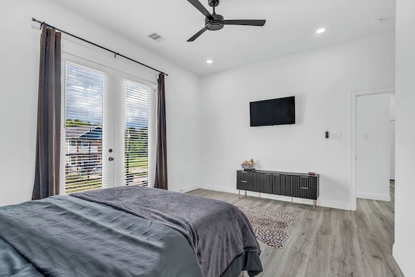 A bedroom with a bed, a ceiling fan, a TV mounted on the wall, and a sliding door leading to a balcony. - The Emerald Noir (Houston)