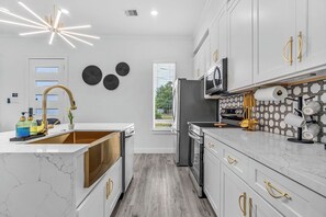A modern kitchen with white cabinetry, gold handles, and a marble countertop. - The Emerald Noir (Houston)