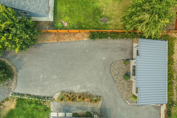 An aerial view of a residential property with a paved driveway, a small garden area, and a building with a grey roof.