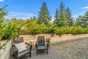 An outdoor seating area with two chairs and a small table, surrounded by a low wall and dense greenery. - Ski Hill Getaway | Modern 1BR, 1.2 Miles to Downtown (Leavenworth)