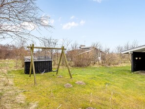 A grassy outdoor area with a wooden swing set, a black shed, and a building with a garage in the background.