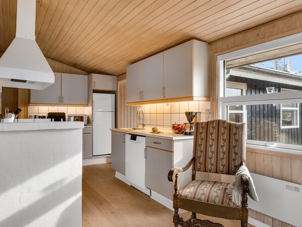 A modern kitchen with white cabinetry, a wooden ceiling, and a large window.