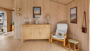Een kamer met houten lambrisering, een houten kast, een stoel met kussen en een klein krukje.
