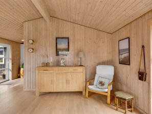 Ein Zimmer mit Holzwänden, einem Holzschrank, einem Sessel mit Kissen und einem kleinen Hocker.