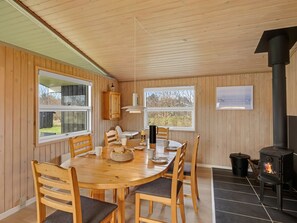 A wooden interior with a round dining table, chairs, a black stove, and windows.