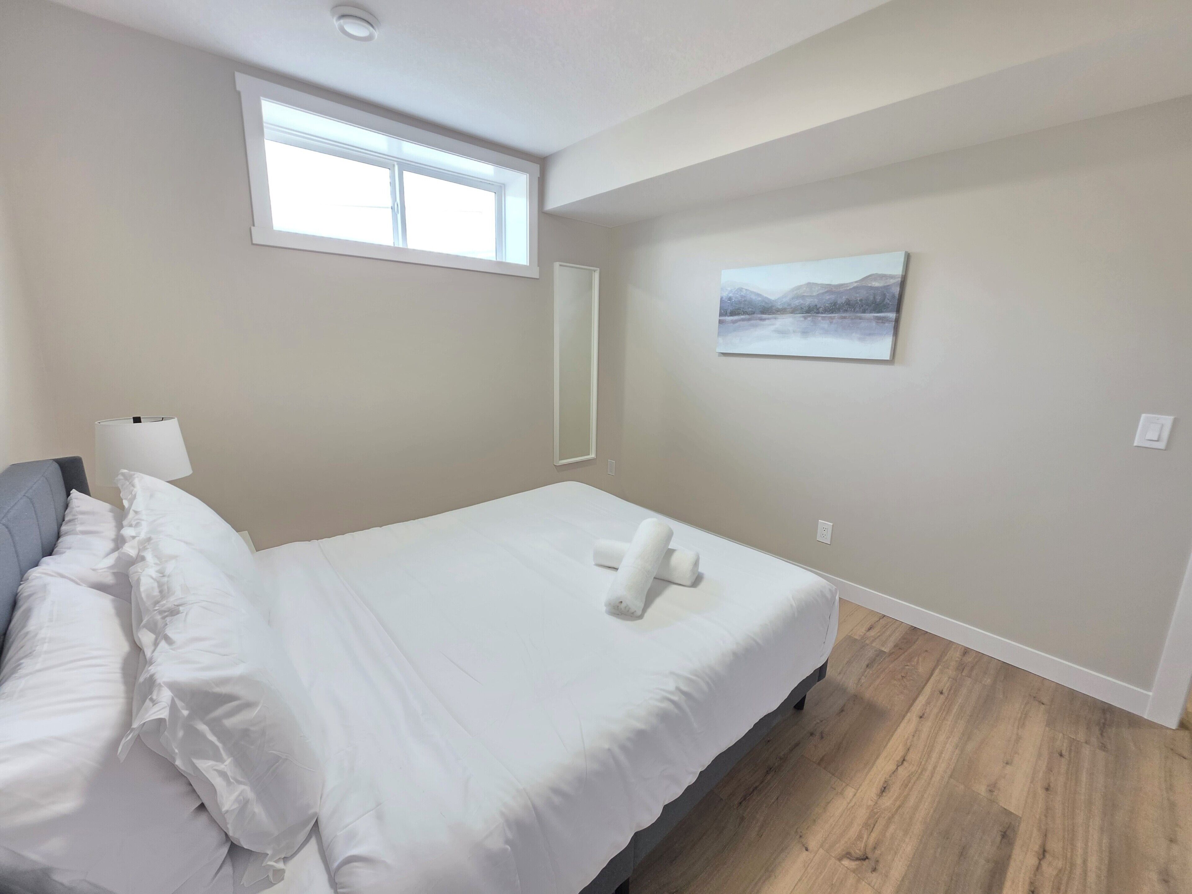 Et hotelværelse med en seng, et vindue, et billede og en lampe.