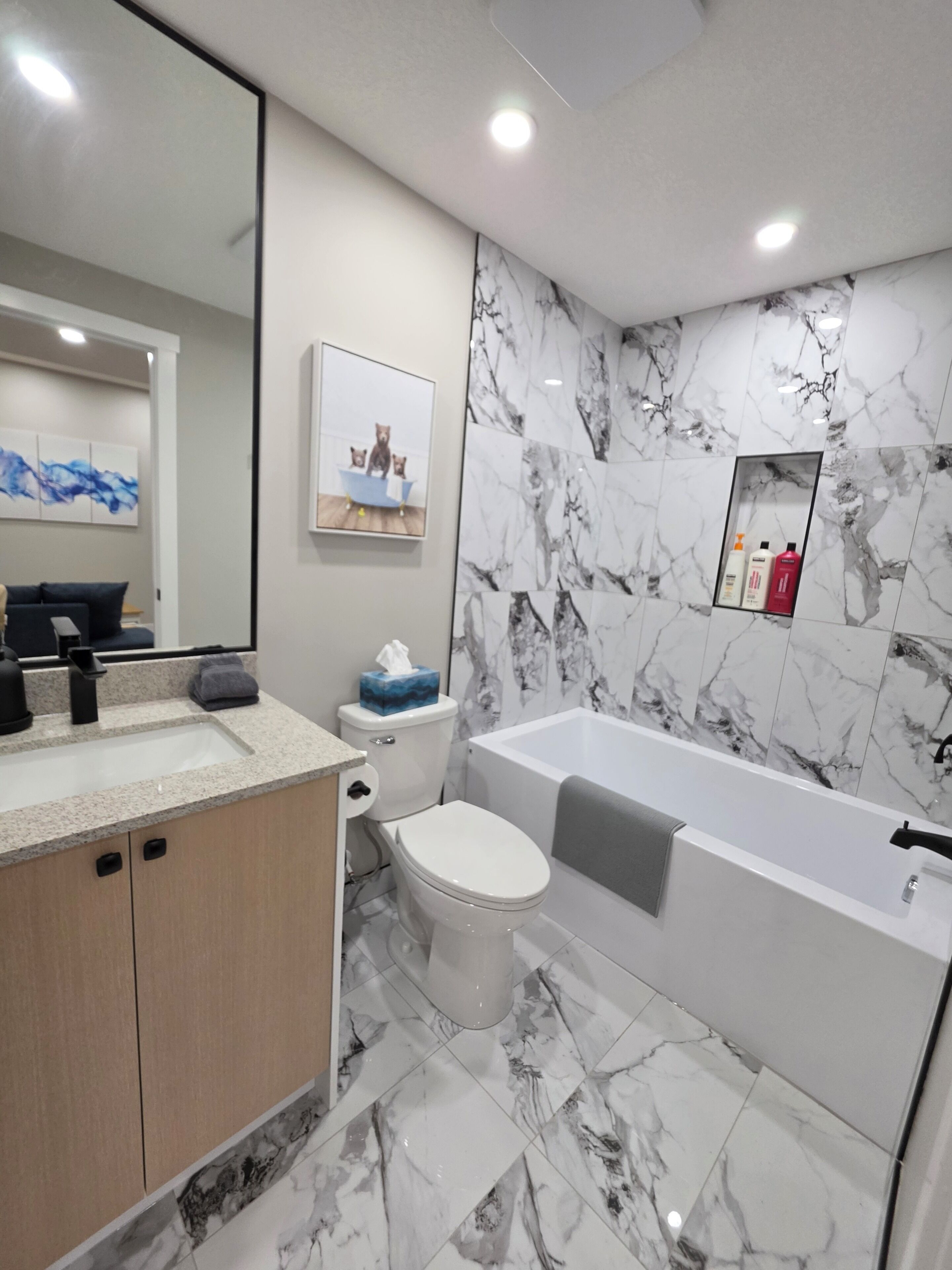 A modern bathroom with a marble floor, a bathtub, a toilet, and a sink.