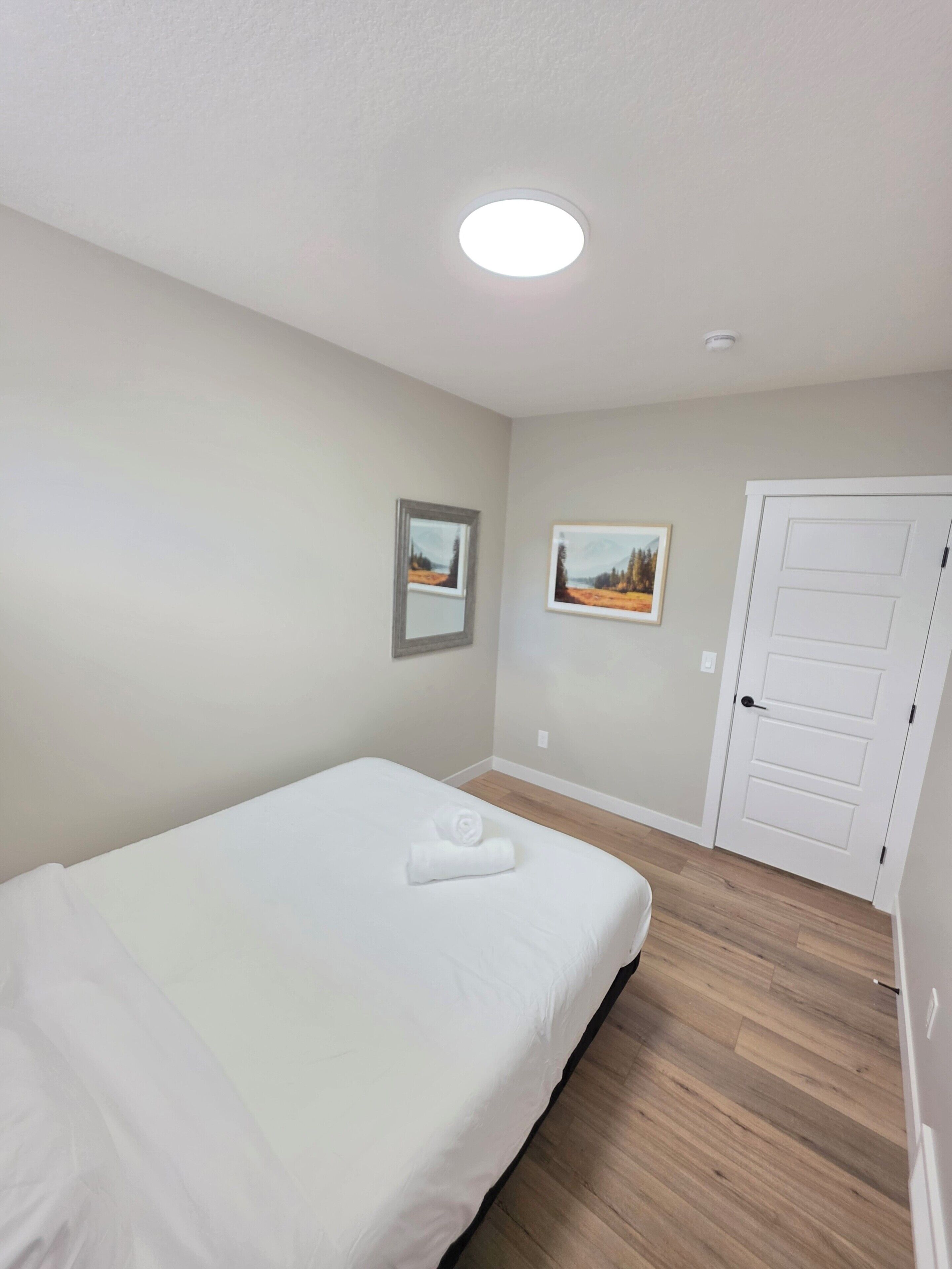 A bedroom with a single bed, a door, and two framed pictures on the wall.
