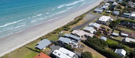 An aerial view of a coastal residential area with houses, a beach, and a road.