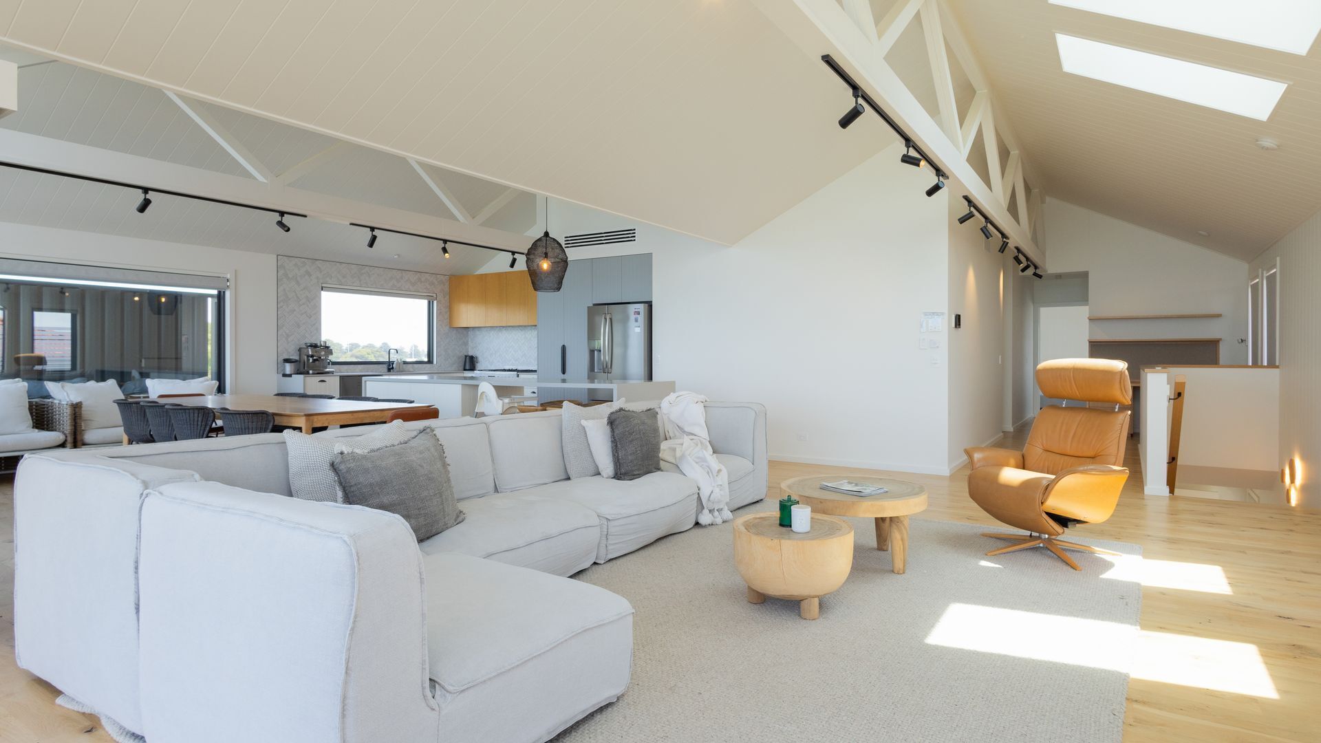 A spacious living area with a large white sectional sofa, a round coffee table, and a leather armchair.