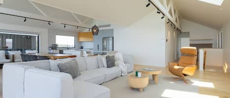 Een ruime zithoek met een grote witte modulaire bank, een ronde salontafel en een leren fauteuil.