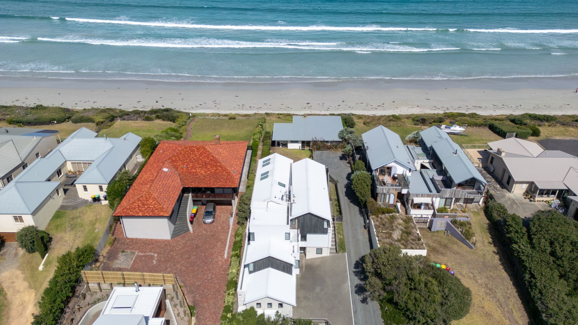 Vue aérienne d’une zone résidentielle côtière, avec des maisons, une plage et un ciel dégagé.