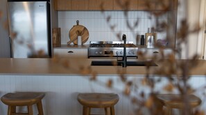 A modern kitchen with a stainless steel stove, wooden bar stools, and a tiled backsplash. - Salt At East - Top Floor (Port Fairy)