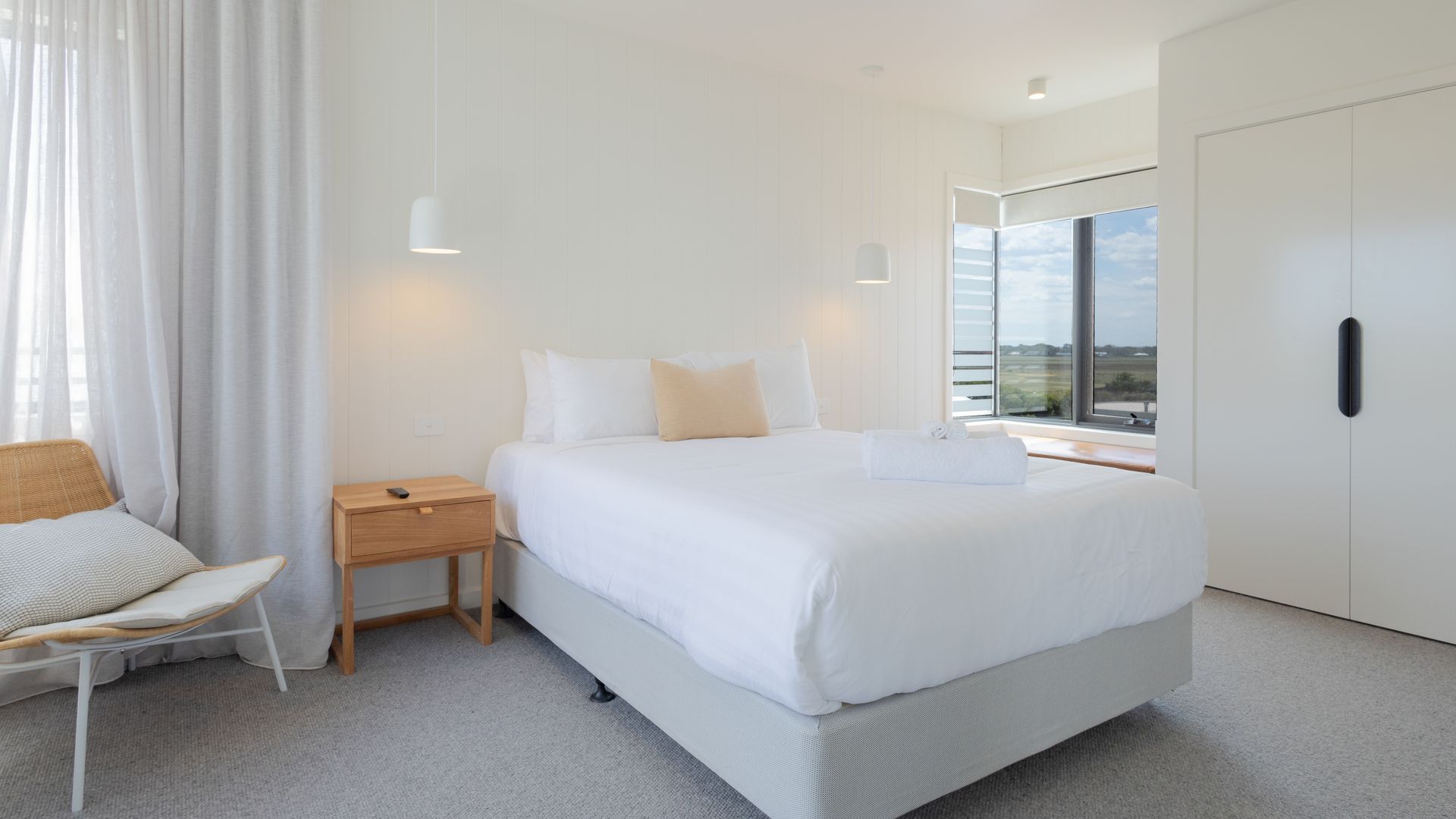 A modern bedroom with a large bed, bedside tables, a chair, and a wardrobe.