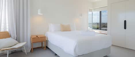 A modern bedroom with a large bed, bedside tables, a chair, and a wardrobe.