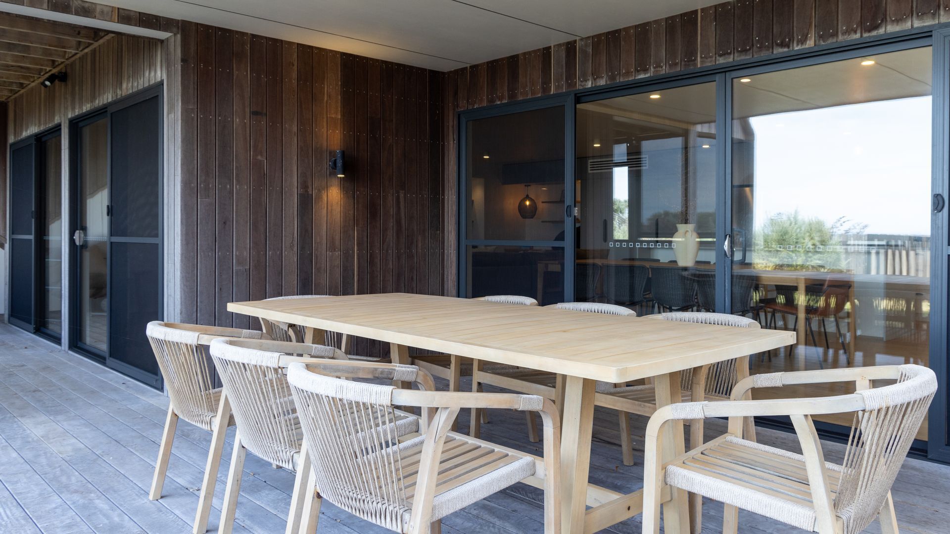 Une terrasse en bois avec une table et des chaises, une porte-fenêtre coulissante et une vue sur l’extérieur.