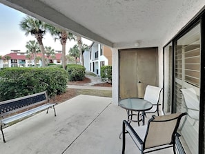 Ein Balkon mit einer Bank und einem Tisch, der auf eine angelegte Grünfläche mit Palmen und einem Gebäude im Hintergrund blickt.