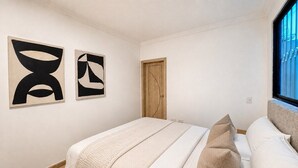 Ein Schlafzimmer mit Bett, Kissen, einer Holztür und abstrakter Kunst an der Wand.