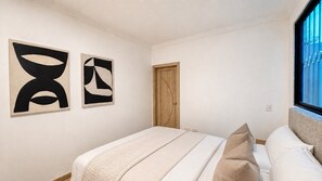 Ein Schlafzimmer mit Bett, Kissen, einer Holztür und abstrakter Kunst an der Wand.