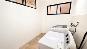 Een wasserette met een wasmachine en droger, een raam met zonwering, en een betegelde vloer.