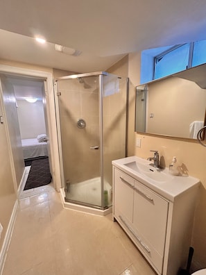 Ein modernes Badezimmer mit einer Glaskabine zur Dusche, einem weißen Waschbecken und einem Spiegel darüber.