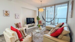 A modern living room with a flat-screen TV, comfortable seating, a glass coffee table, and a large window with a view. - Amazing experience with ocean views on Balboa Ave 2 (Panamá)