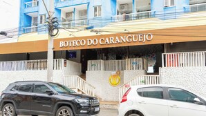 En byggnad med en skylt där det står ”Boteco do Caranguejo” och en logotyp med en snigel. Två bilar står parkerade framför.