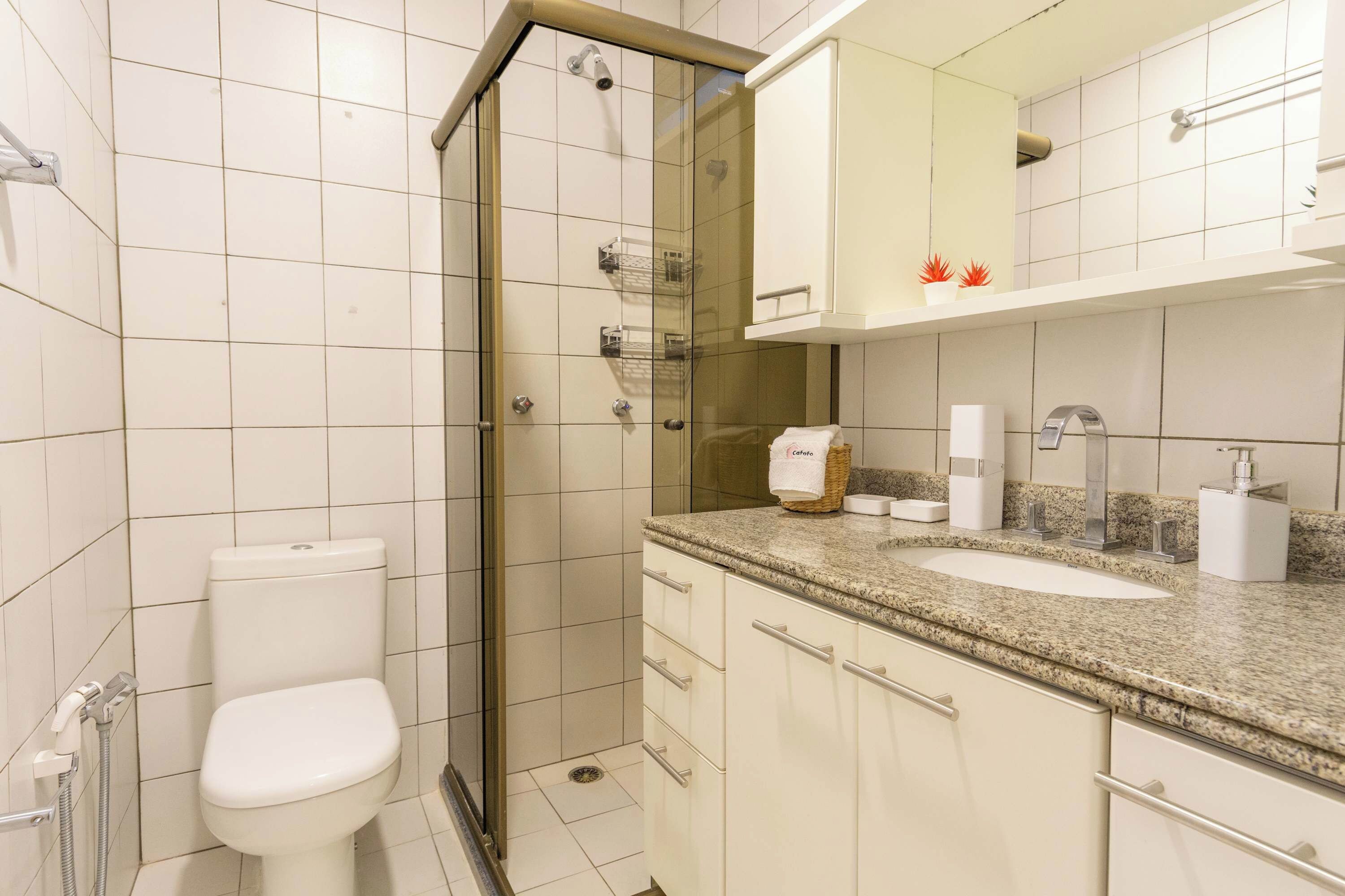 A bathroom with a toilet, a shower with a glass door, a sink with a granite countertop, and a mirror above the sink.