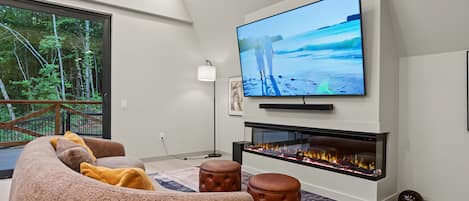 Ett modernt vardagsrum med en platt-TV, en öppen spis, en soffa och ett matbord.