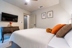 Une chambre d’hôtel avec un lit, un téléviseur fixé au mur, une porte et deux tableaux encadrés.
