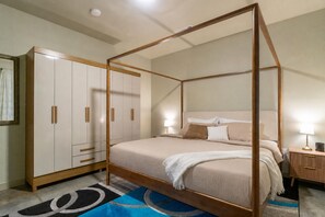 Ein Bett mit Baldachin, dessen Holzrahmen sichtbar ist, ein Nachttisch mit Lampe und ein Kleiderschrank mit mehreren Schubladen.