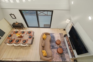 Ein modernes Wohnzimmer mit Essbereich, einer Couch, einem Flachbildfernseher und einem großen Fenster mit Blick auf ein Gewässer.