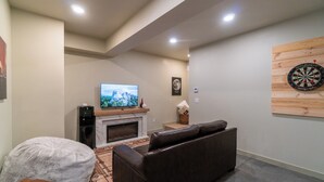 A living room with a fireplace, a television, a dartboard, and a couch. - AlpenDorf A-Frame— new! one-of-a-kind luxury a-frame, dog friendly, natural creek, mins from Helen (Sautee Nacoochee)