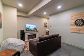 A living room with a fireplace, a television, a dartboard, and a couch. - AlpenDorf A-Frame— new! one-of-a-kind luxury a-frame, dog friendly, natural creek, mins from Helen (Sautee Nacoochee)