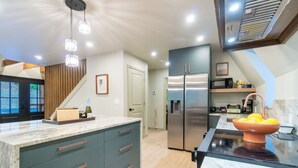 A modern kitchen with a central island, stainless steel appliances, and a wooden staircase. - AlpenDorf A-Frame— new! one-of-a-kind luxury a-frame, dog friendly, natural creek, mins from Helen (Sautee Nacoochee)