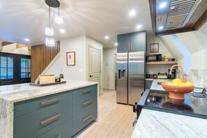 A modern kitchen with a central island, stainless steel appliances, and a wooden staircase. - AlpenDorf A-Frame— new! one-of-a-kind luxury a-frame, dog friendly, natural creek, mins from Helen (Sautee Nacoochee)