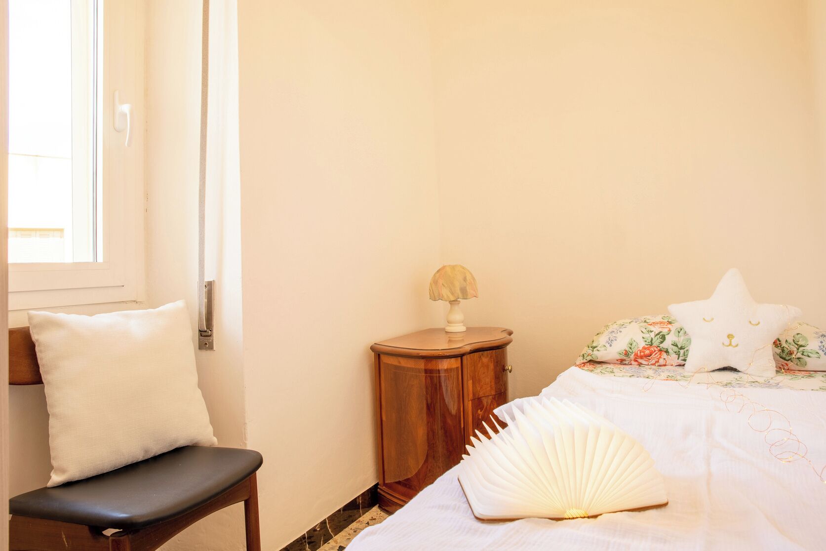 Un dormitorio con cama, una mesita de noche con lámpara, una silla y un ventanal.