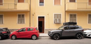 A street view with parked cars, a building with balconies, and a door with shutters. - Sun and Sea - Alghero (Alghero)